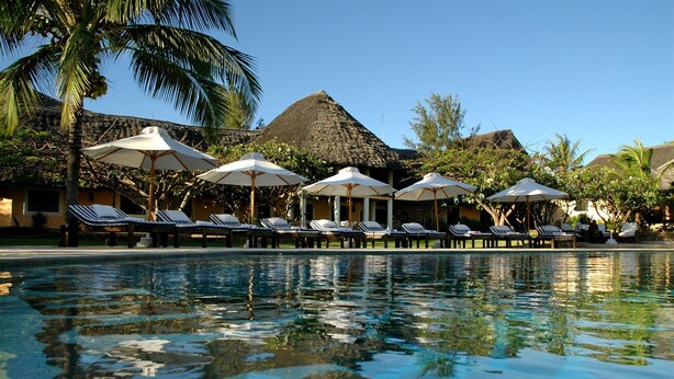 A pool area with lounge chairs and umbrellas, surrounded by palm trees and thatched-roof structures. - Lion In The Sun Hotel (Malindi)