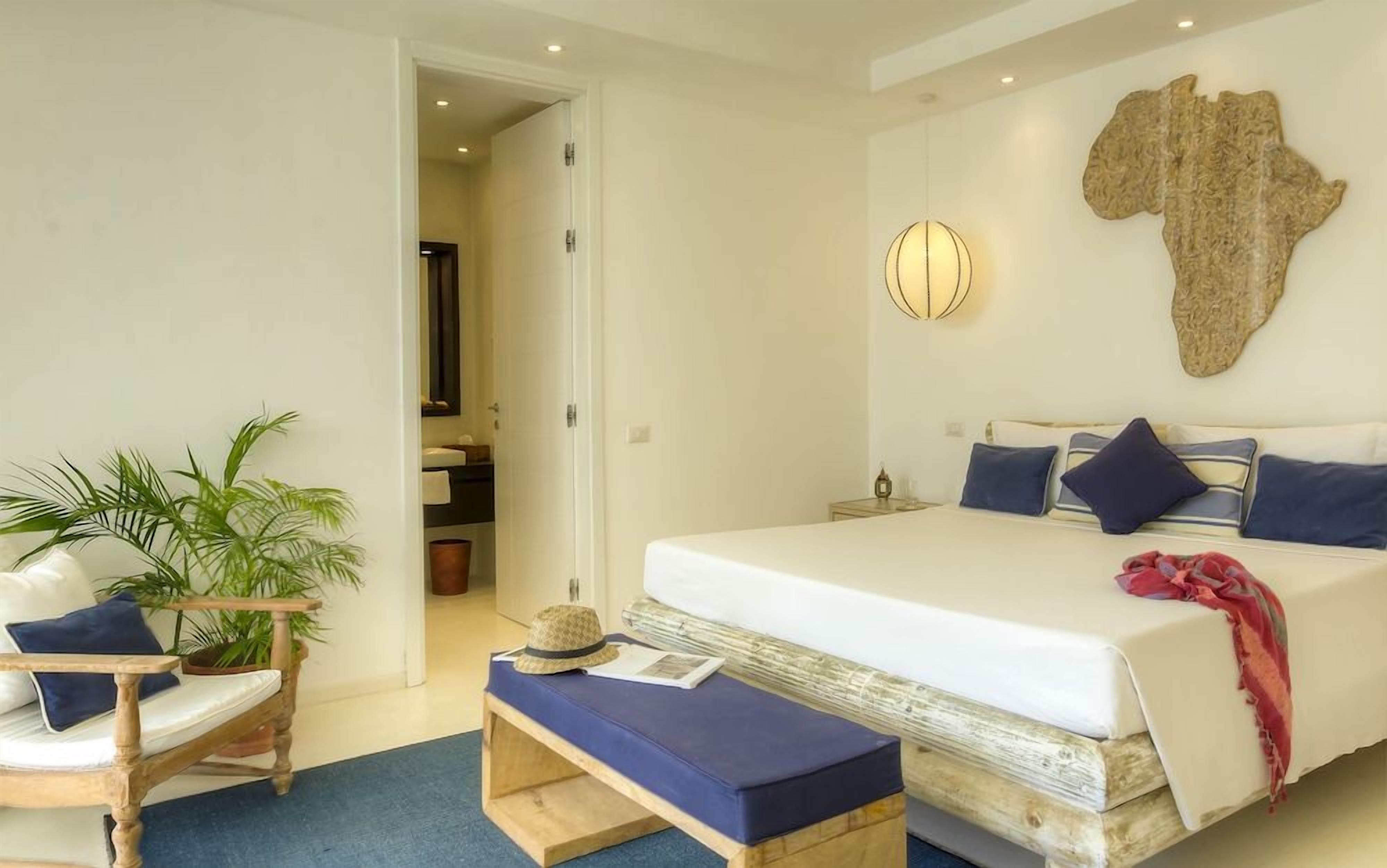 A bedroom with a large bed, a bedside table, a wall-mounted light, and a map decoration.