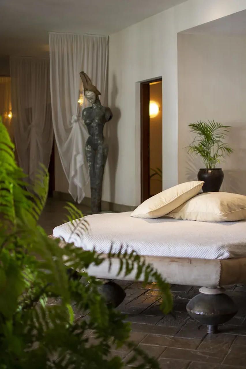 A bedroom with a bed, a potted plant, a statue, and a curtain.