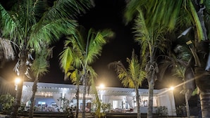 A nighttime view of a beachside hotel with palm trees and a covered outdoor dining area. - Lion In The Sun Hotel (Malindi)