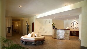A hotel lobby with a reception desk, a reception area, and a seating area with a sofa and decorative pillows. - Lion In The Sun Hotel (Malindi)