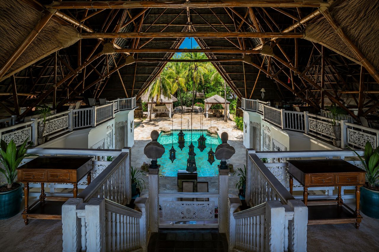 A pool area with a thatched roof, surrounded by white railings and potted plants.