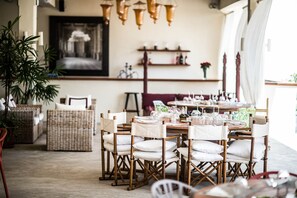 Uma sala de jantar com móveis de vime, uma mesa posta com copos e um lustre.