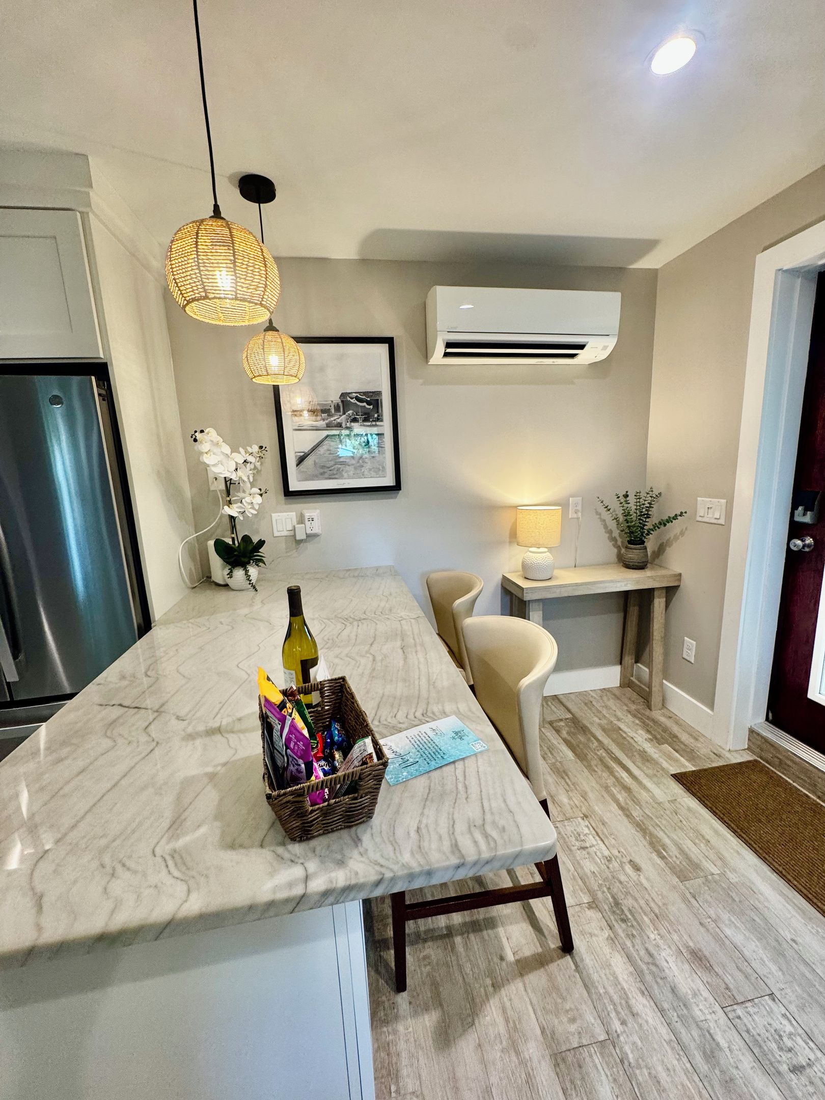 A modern kitchen with a marble countertop, pendant lights, an air conditioning unit, and a dining area with a chair and table.