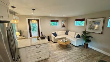 A modern living room with a sectional sofa, a coffee table, and a kitchen area with a refrigerator.