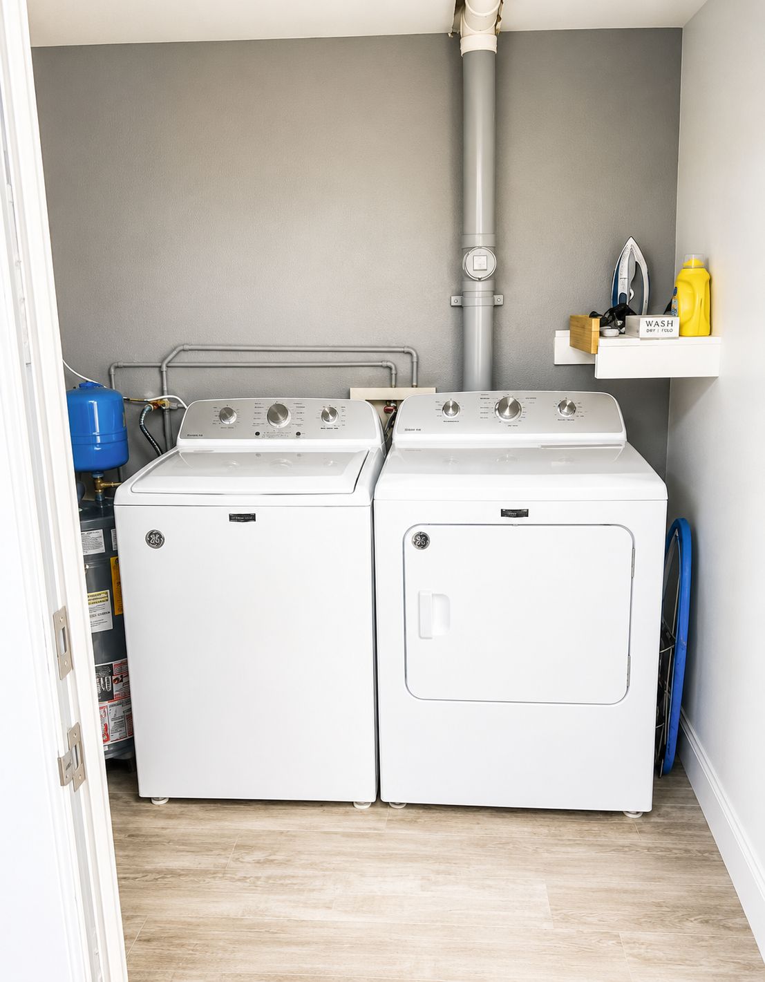 A laundry room with two front-loading washing machines, a water heater, and a shelf with laundry supplies.