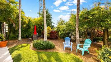 A garden with palm trees, a red umbrella, and two blue chairs.