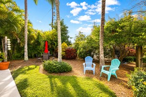 A garden with palm trees, a red umbrella, and two blue chairs. - Private Cottage | Walk to Beach, Tropical Setting (Delray Beach)