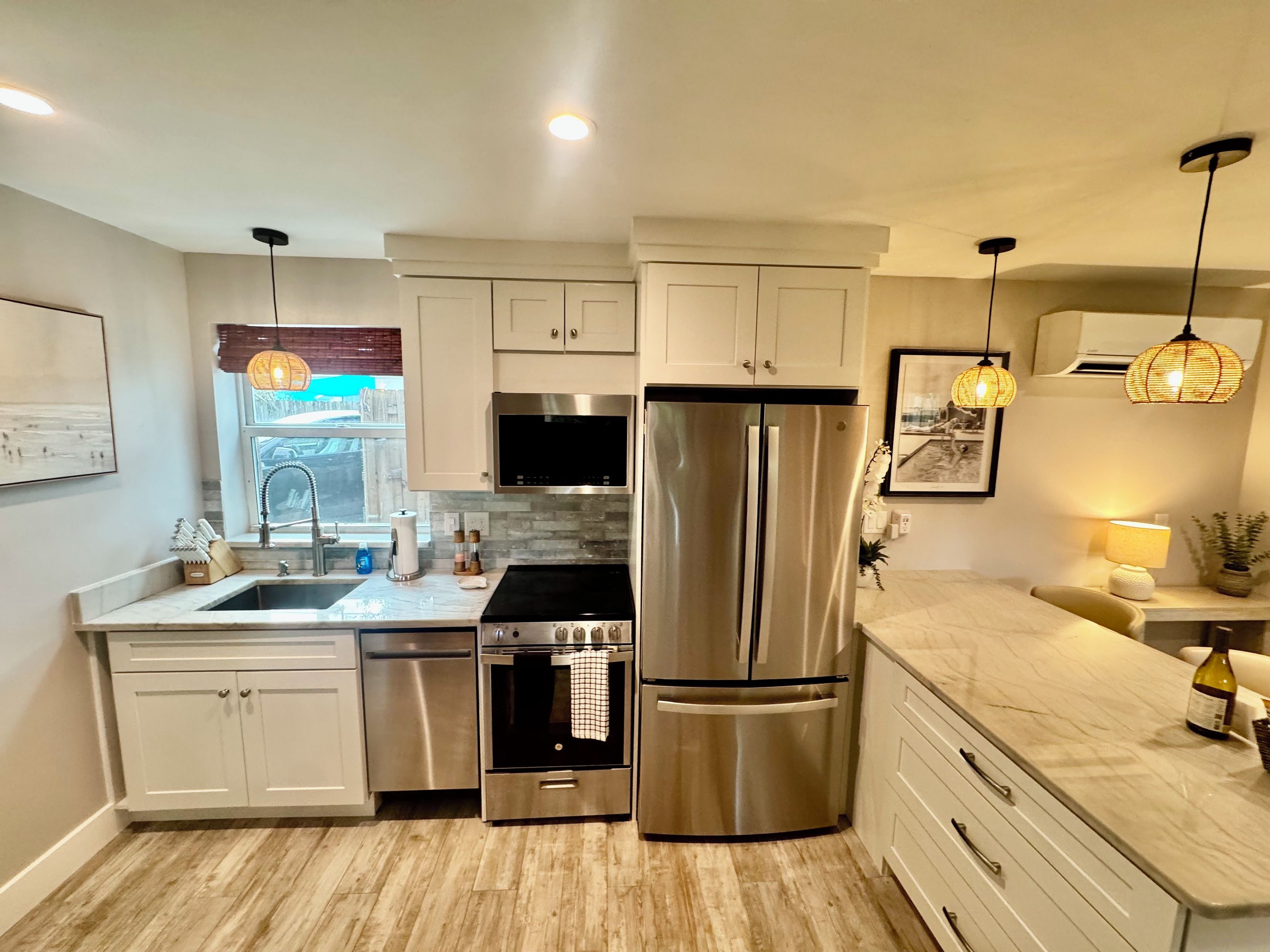 A modern kitchen with stainless steel appliances, white cabinetry, and pendant lighting.