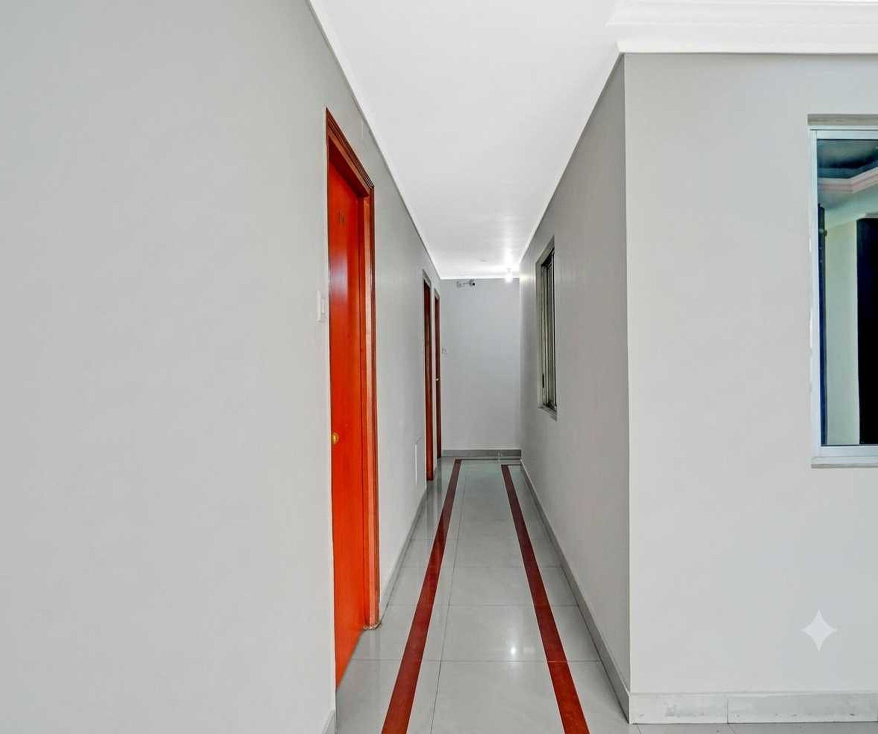 Un corridoio con pareti bianche e una striscia rossa sul pavimento, che conduce a una porta con una finestra.
