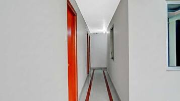 Un corridoio con pareti bianche e una striscia rossa sul pavimento, che conduce a una porta con una finestra.
