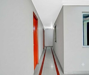 A corridor with white walls and a red stripe on the floor, leading to a door with a window. - Classic Hotel Blue Velvet (Danapur)