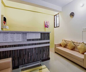A reception area with a reception desk, a sofa, and a wall clock. - Classic Hotel Blue Velvet (Danapur)