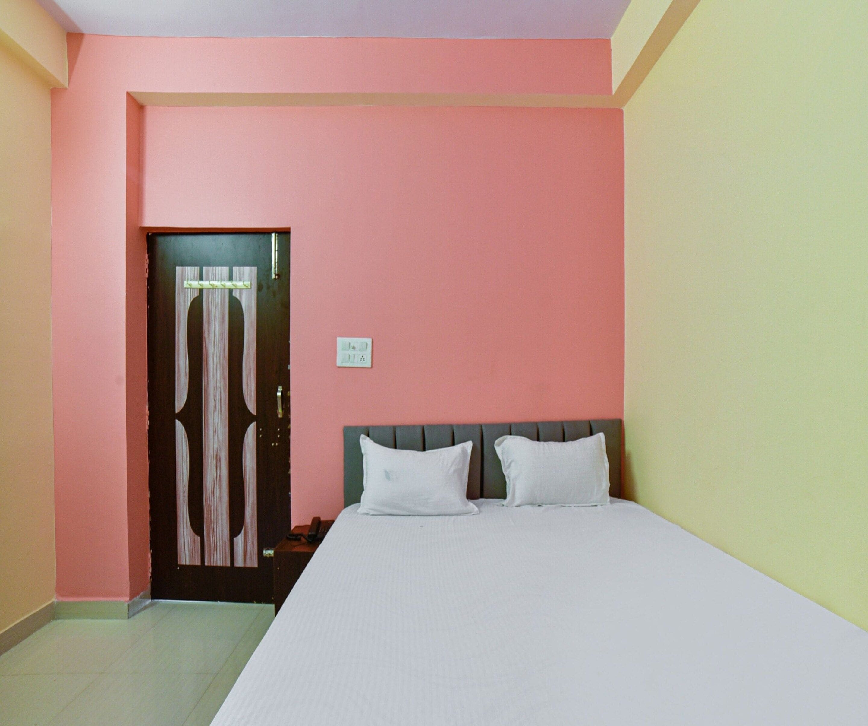 A bedroom with a bed, a nightstand, a door, and a wall switch.