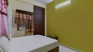 A bedroom with a bed, a wardrobe, a window with curtains, and a small table.