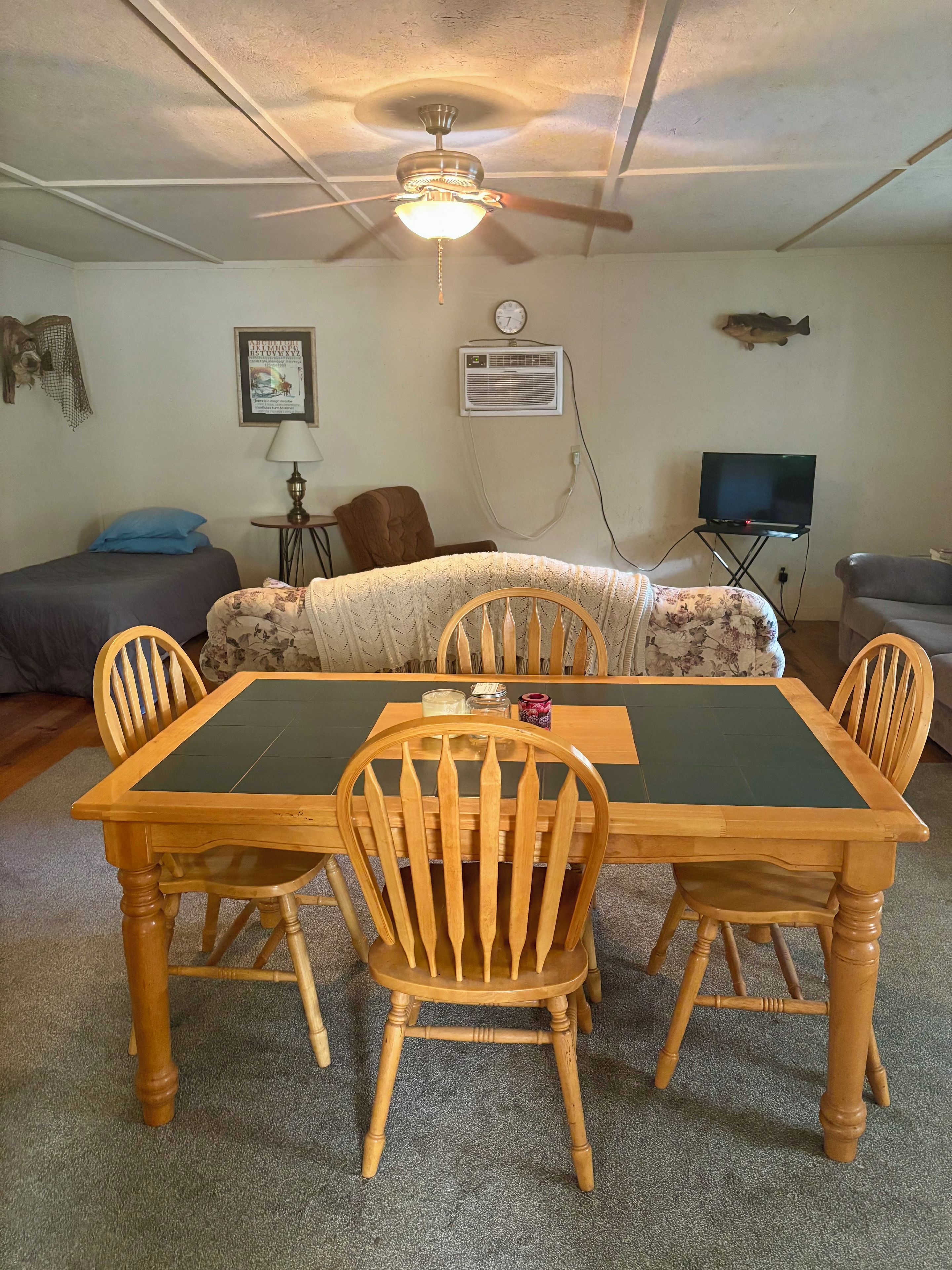A dining area with a wooden table and chairs, a ceiling fan, a clock, and a television on a stand.