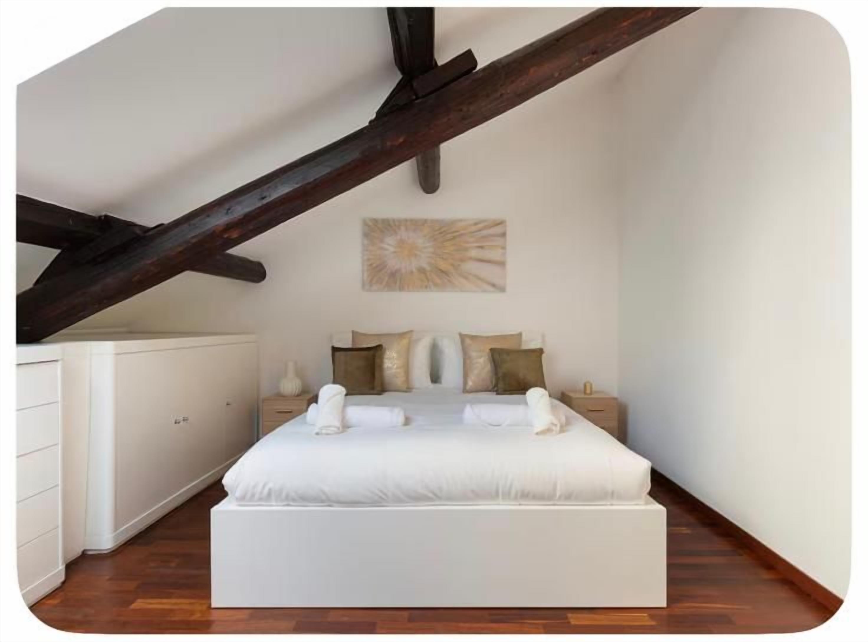 A bedroom with a large bed, a nightstand, a dresser, and a painting on the wall.