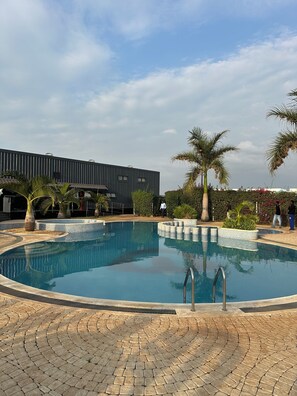 A swimming pool with a tiled deck, palm trees, and a modern building in the background.
