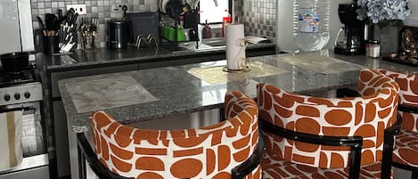 A modern kitchen with a central island, bar stools, and a view of the outdoors.