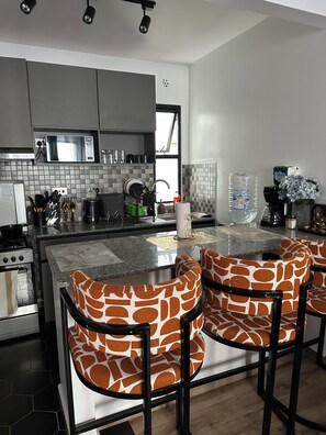 A modern kitchen with a central island, bar stools, and a view of the outdoors.