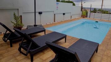 Une piscine sur le toit, avec des chaises longues et un pot de fleurs.