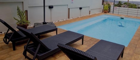 A rooftop swimming pool with lounge chairs and a potted plant.