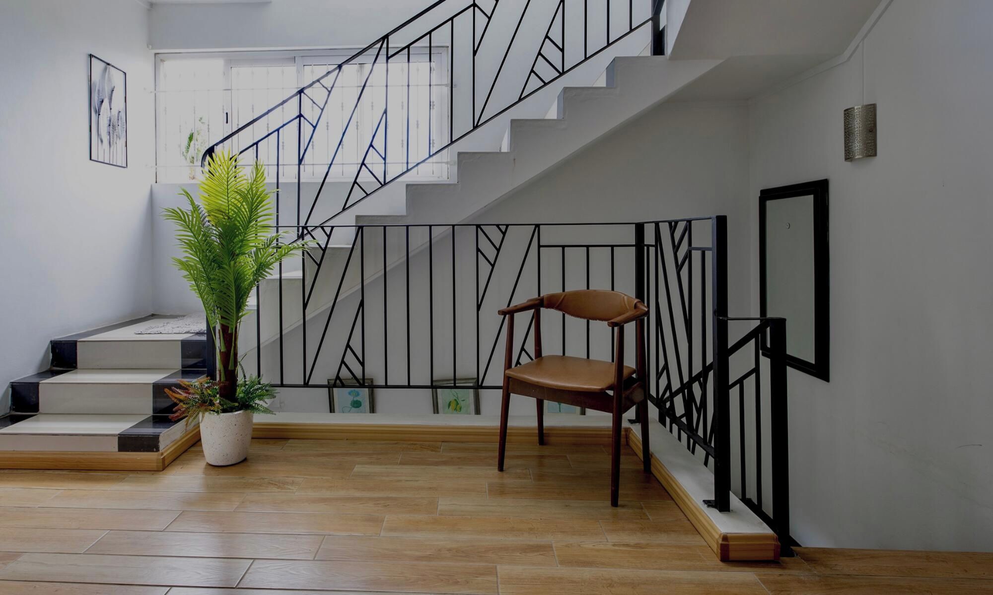 Un escalier avec une rampe en métal noir, une plante en pot et un fauteuil marron dans un espace intérieur moderne.