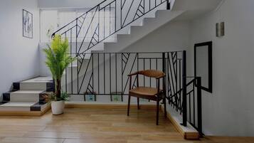 Un escalier avec une rampe en métal noir, une plante en pot et un fauteuil marron dans un espace intérieur moderne.