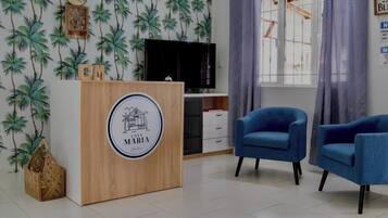 Une pièce avec un comptoir d’accueil en bois, deux fauteuils bleus, un téléviseur et une fenêtre avec des rideaux.