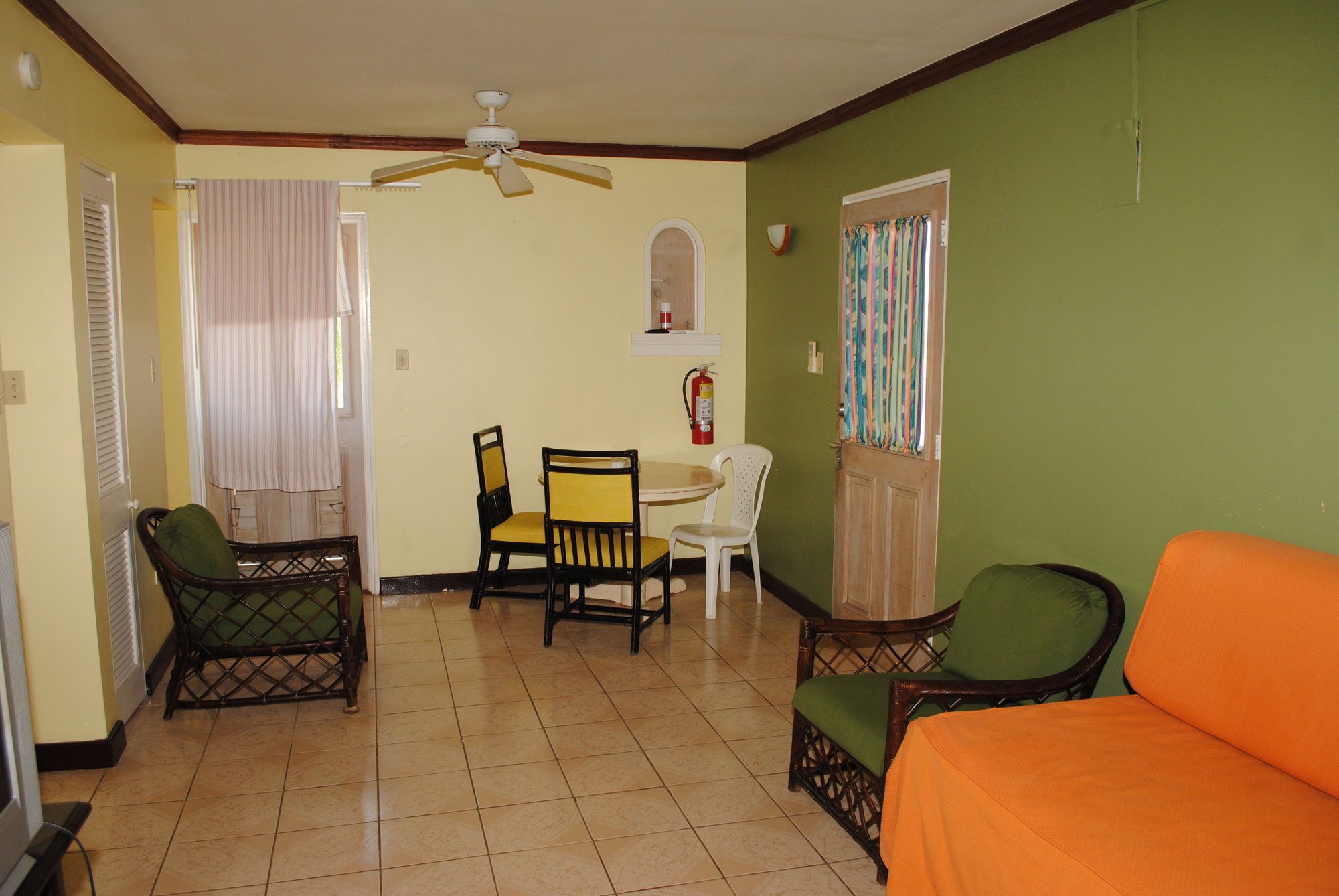 A living room with a ceiling fan, a dining table with chairs, a sofa, and a window with curtains.