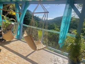 Uma varanda com duas redes, vista para uma paisagem montanhosa e plantas em vasos.