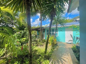 Um jardim tropical com um caminho que leva a um edifício com fachada azul-turquesa e porta branca.