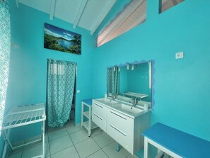 Casa de banho com parede azul, duas pias, um espelho e cortina de chuveiro.