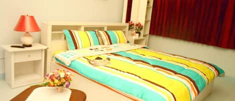 Un dormitorio con cama, mesitas de noche, una silla, una lámpara, una ventana con cortinas y un cuadro colgado en la pared.