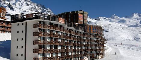 A multi-story hotel with balconies, situated in a snowy mountainous area.