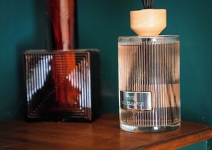 A clear glass bottle with a wooden cap and a label, placed on a wooden surface against a teal background.