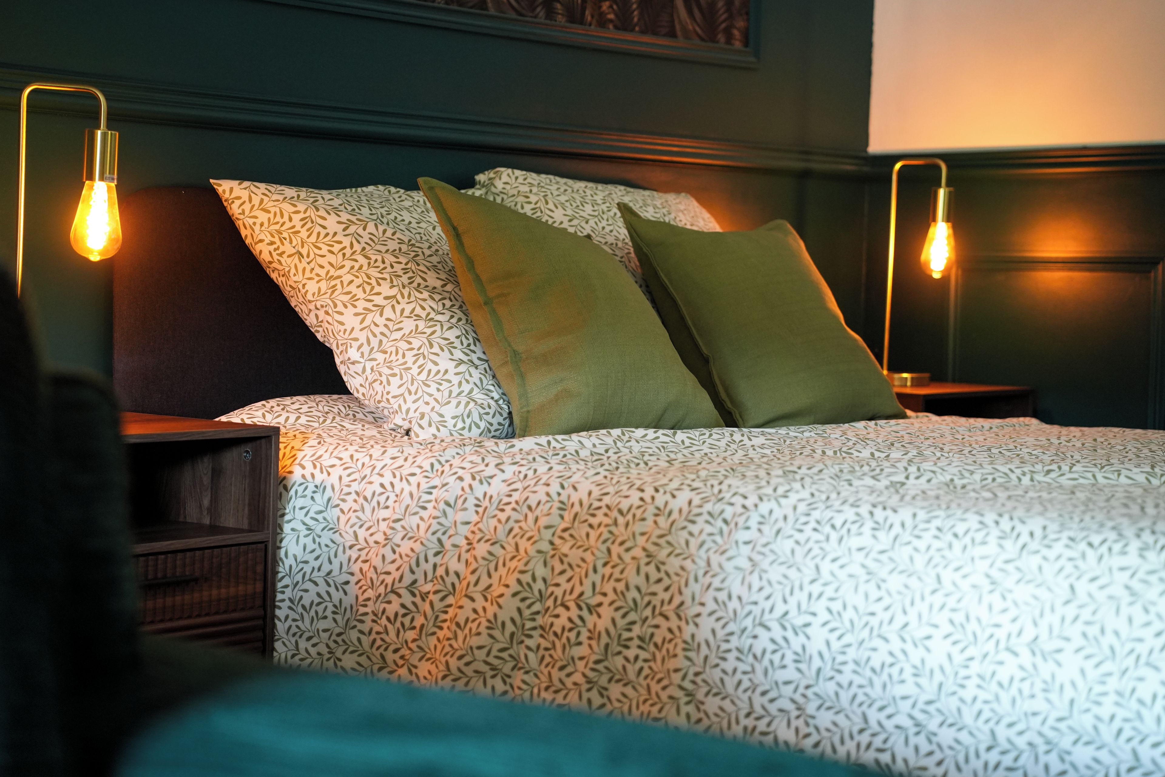 A neatly made bed with patterned bedding, two bedside lamps, and a dark headboard.