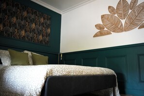 Une chambre à coucher avec un lit, des oreillers, un mur orné d’un motif de feuilles et un mur de couleur vert foncé.