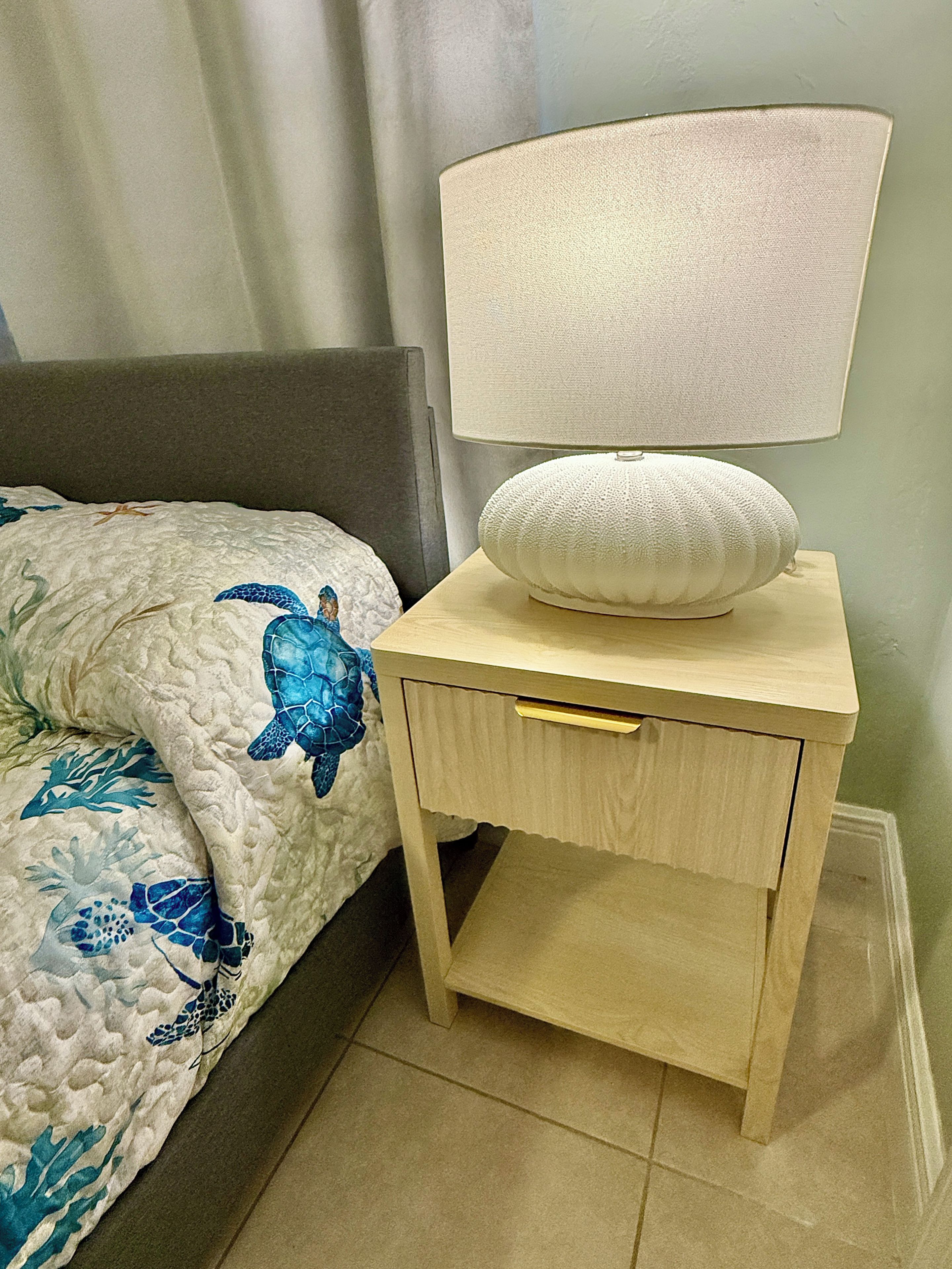 Una cama con diseño de tortuga marina azul, una lámpara de noche y una mesita de noche de madera con cajón.