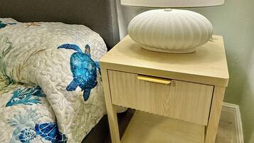 Una cama con diseño de tortuga marina azul, una lámpara de noche y una mesita de noche de madera con cajón.