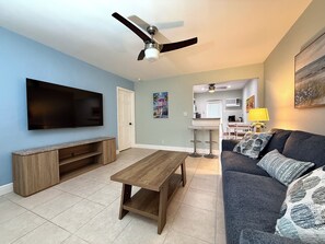 A living room with a flat-screen TV, a wooden coffee table, a ceiling fan, and a sofa with patterned cushions.