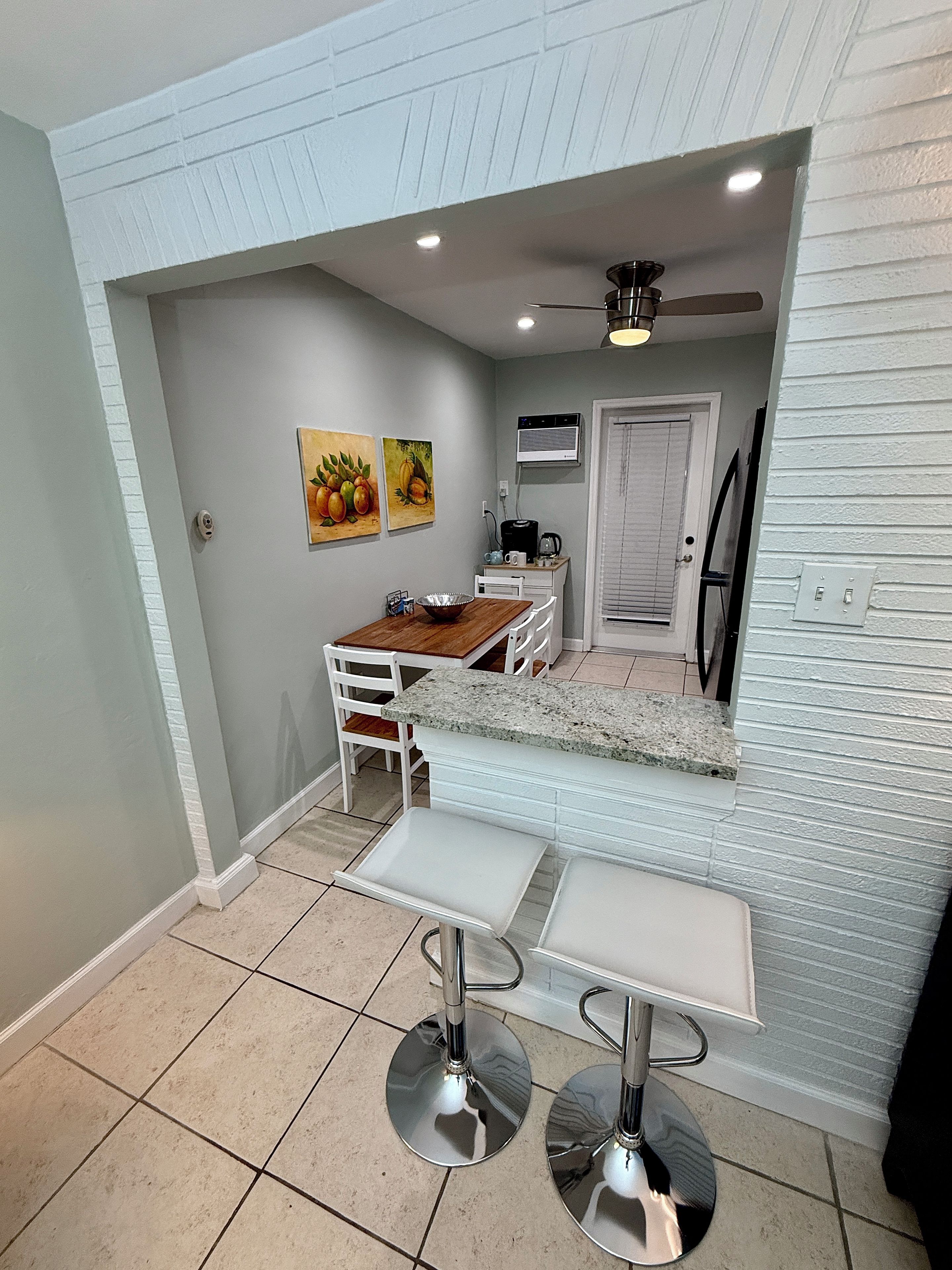 A compact kitchen with a dining area, featuring a white countertop, a ceiling fan, and a wall-mounted air conditioner.