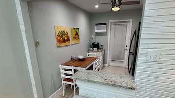 A compact kitchen with a dining area, featuring a white countertop, a ceiling fan, and a wall-mounted air conditioner.