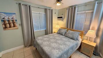 A bedroom with a bed, a ceiling fan, a nightstand with a lamp, and a wall-mounted air conditioner.