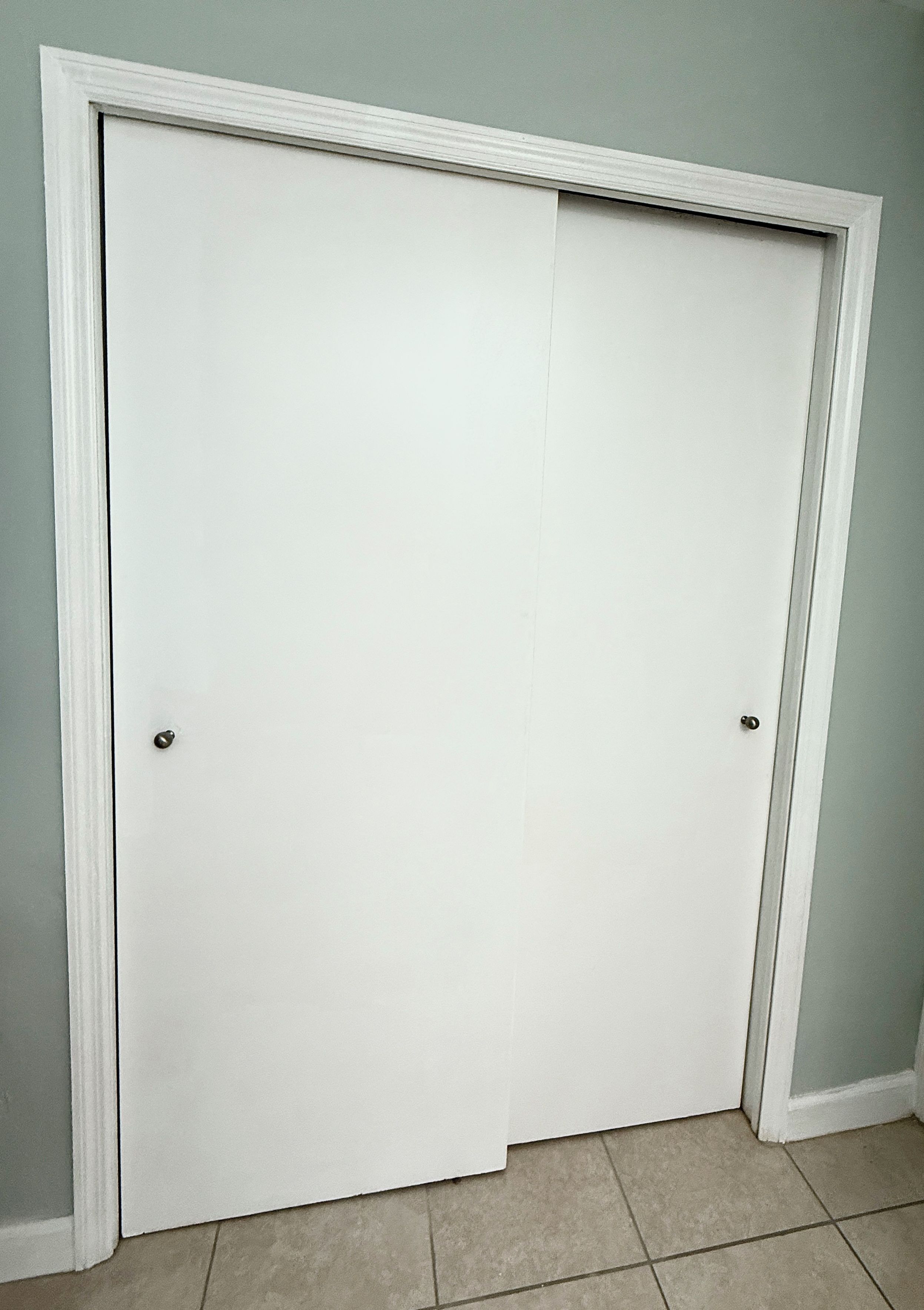 A closed white door with a simple handle, set in a room with light-colored walls and a tiled floor.