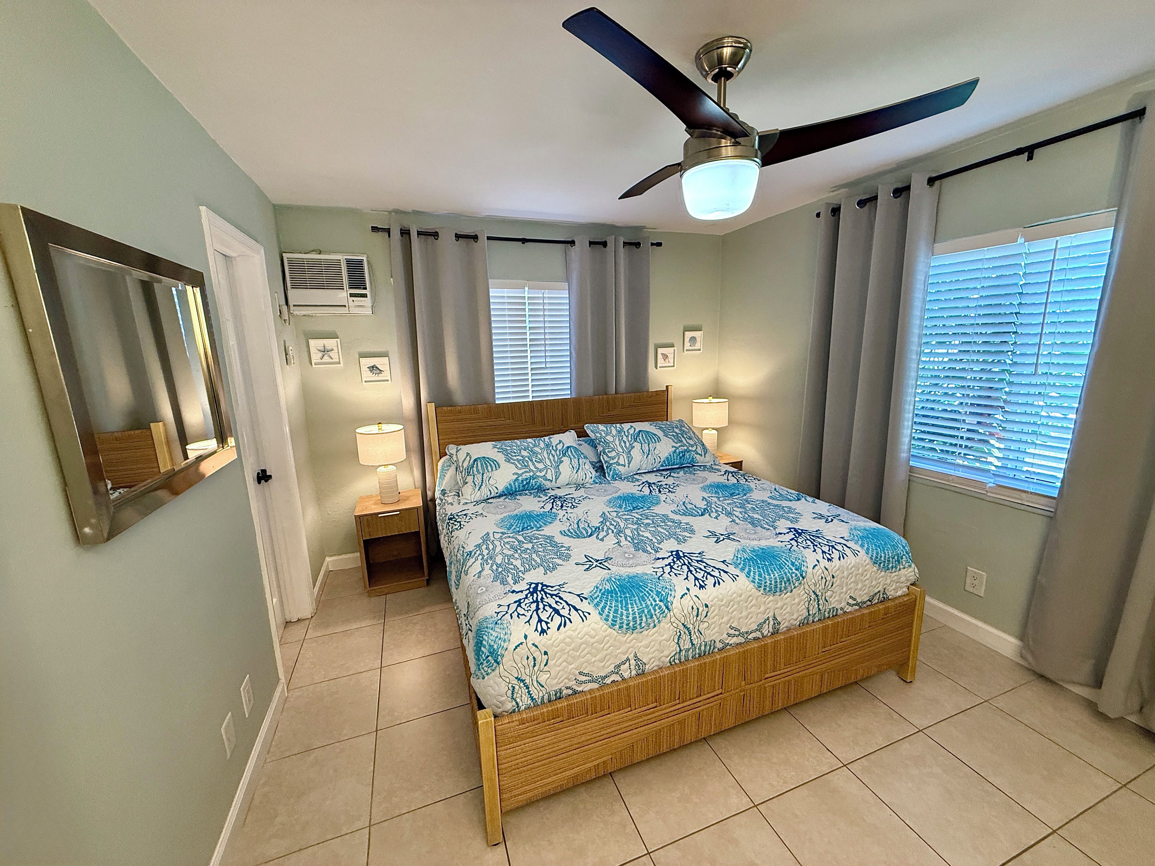 A bedroom with a bed, ceiling fan, bedside lamps, and a window with blinds.
