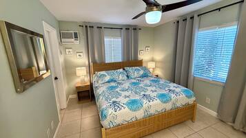 A bedroom with a bed, ceiling fan, bedside lamps, and a window with blinds.
