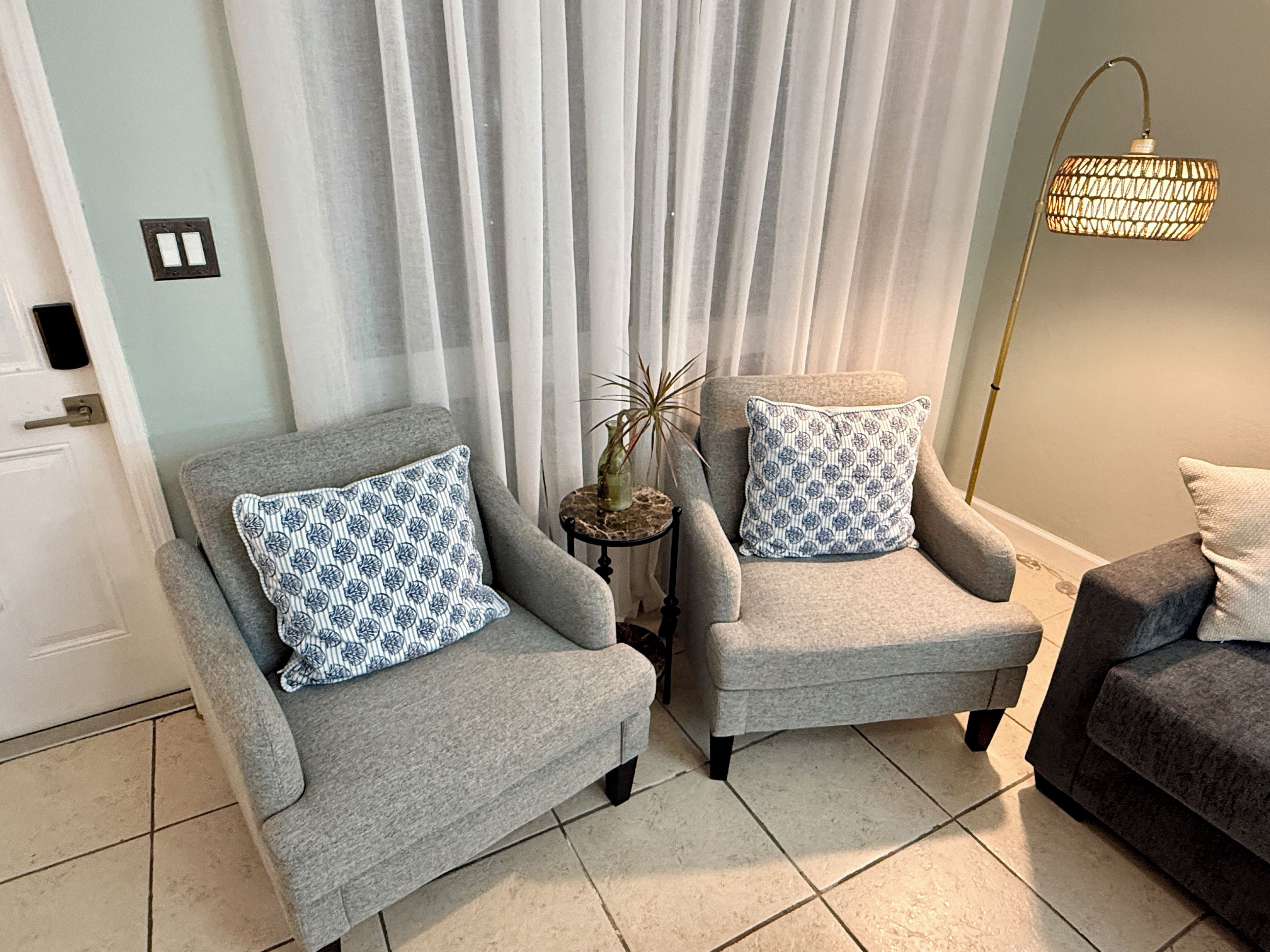 A living room with two grey armchairs, a small side table with a plant, and a floor lamp.