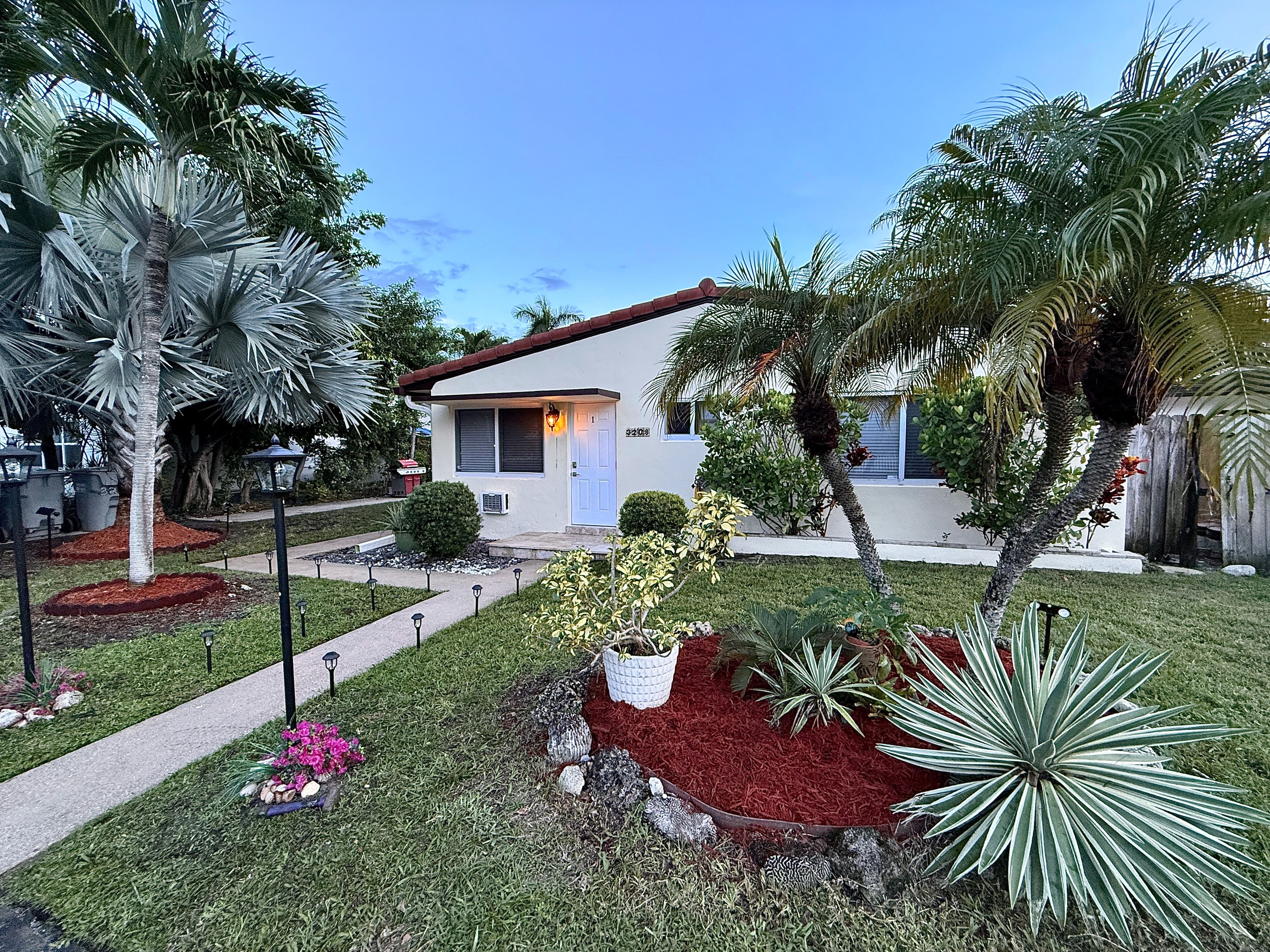 A residential property with a well-maintained lawn, various plants, and a small house with a red roof.