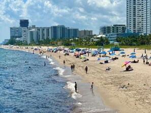 A beach with people swimming and walking along the shore, umbrellas, and beach chairs.